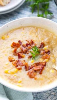 A bowl of creamy potato soup with corn showing bacon crumbles on top and a spoon in the soup.