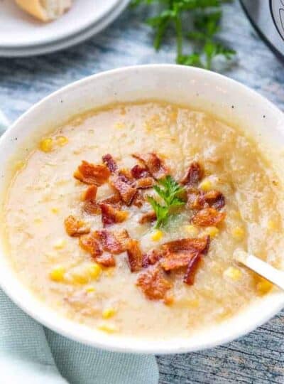 A bowl of creamy potato soup with corn showing bacon crumbles on top and a spoon in the soup.