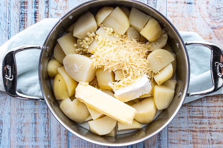 a pot of cut up potatoes with butter, cheese, and cream cheese