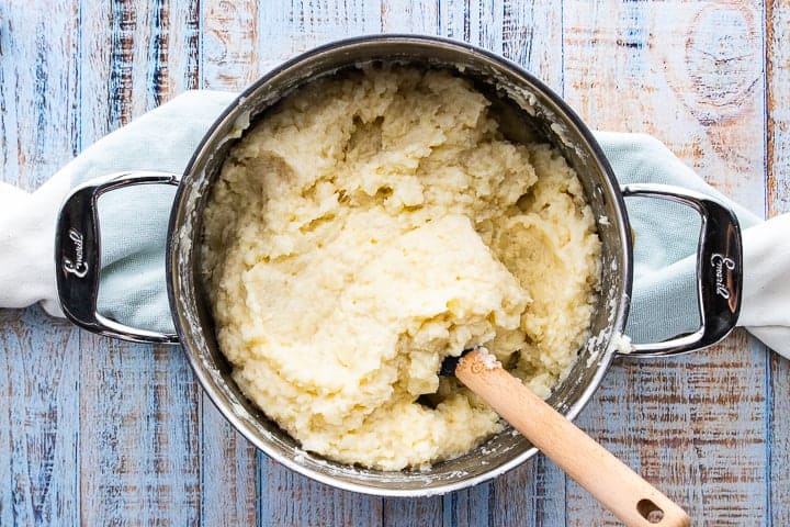 Cheesy Garlic Mashed Potatoes, make ahead mashed potatoes for a crowd, showing mashed potatoes in a stockpot on a wooden surface.