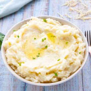 a white bowl with mashed potatoes with melted butter and scallions.