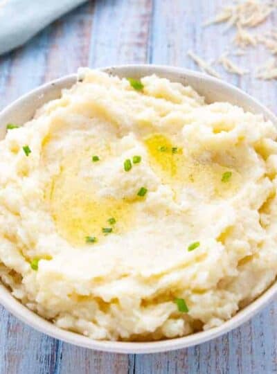a white bowl with mashed potatoes with melted butter and scallions.
