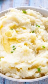 A white bowl filled with mashed potatoes topped with melted butter and scallions.