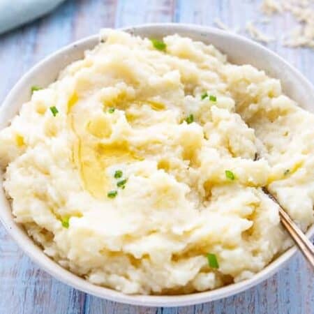 A white bowl filled with mashed potatoes topped with melted butter and scallions.