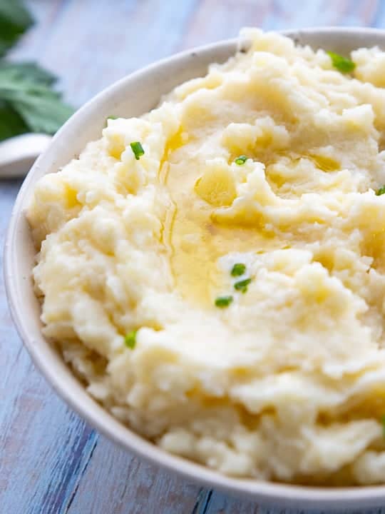 Cheesy Garlic Mashed Potatoes, make ahead mashed potatoes for a crowd, showing a bowl of mashed potatoes on a wooden surface. 