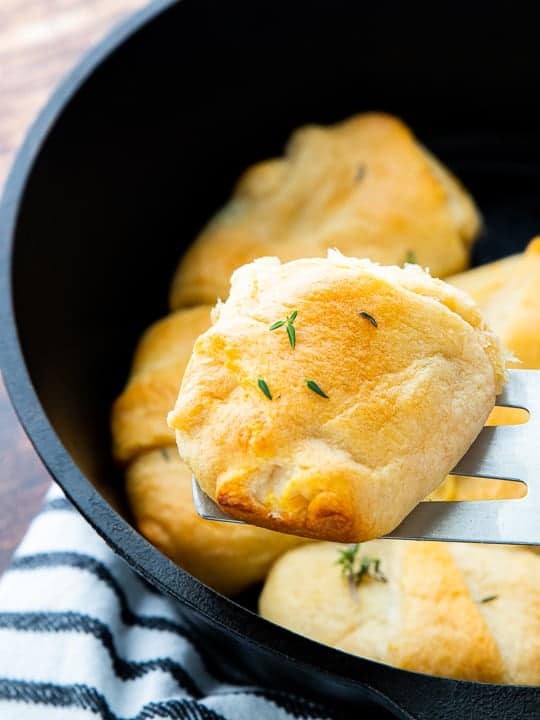 Chicken Pot Pie with Crescent Rolls, a crescent roll chicken pot pie recipe, showing a crescent roll being scooped out of the cast iron skillet.