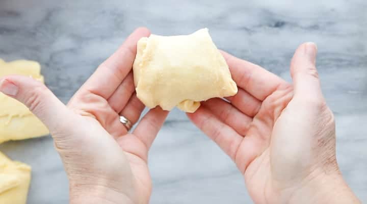 Chicken Pot Pie with Crescent Rolls, a crescent roll chicken pot pie recipe, showing hands holding a crescent roll filled with pot pie filling.