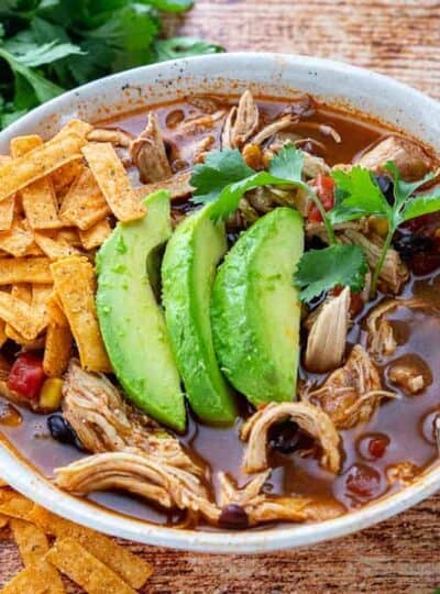 A bowl of chicken tortilla soup in a white bowl with tortilla chips and fresh avocado.
