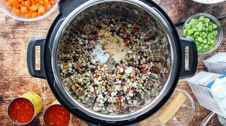 a top down look into an instant pot showing it filled with dry beans with small bowls of ingredients surrounding the instant pot. 