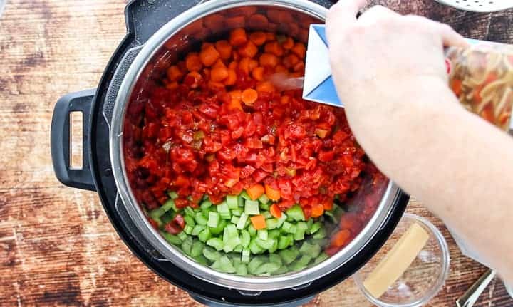 a top down view into an instant pot showing the instant pot filled with vegetables and beans with stock being poured into the pot.