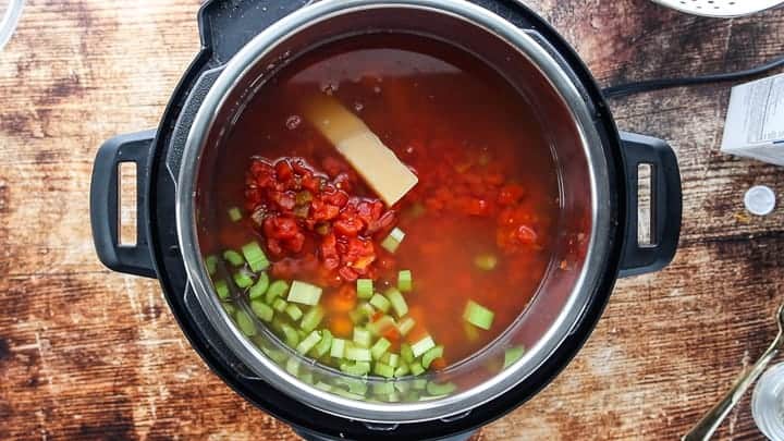 a top down view showing an instant pot filled with stock, beans, vegetables and a parmesan rind.