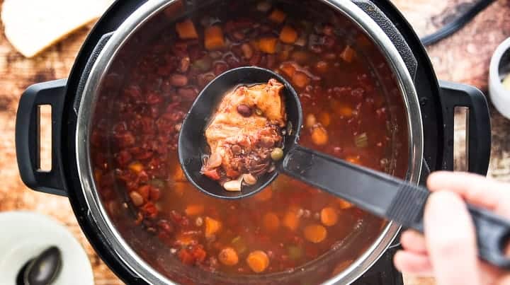 a top down view showing an instant pot filled with soup and a ladle scooping out the parmesan rind. 