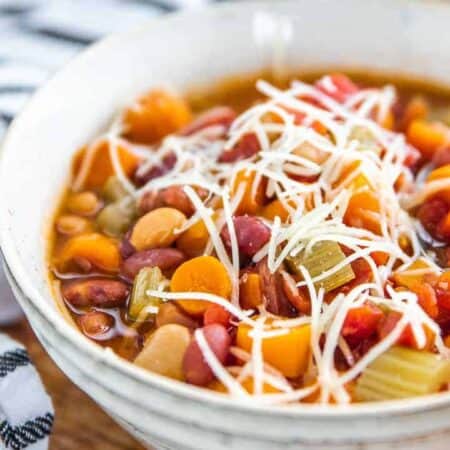 Minestrone soup in a white bowl packed with bean, carrots and celery with shredded cheese on top.
