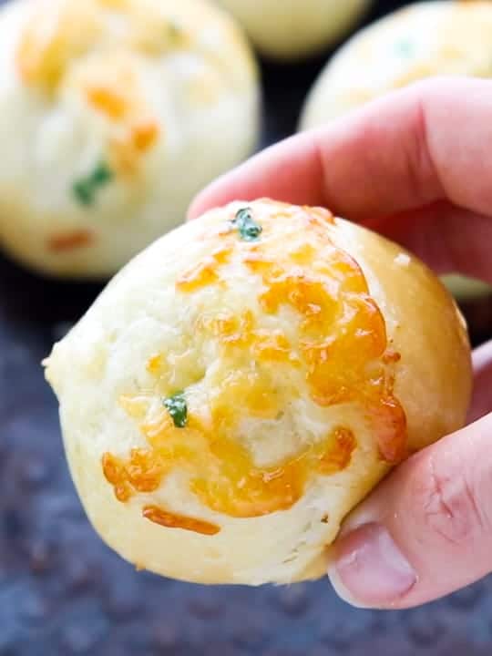 Parmesan Rhodes Rolls, a frozen dinner rolls recipe, showing Rhodes rolls on a baking sheet with a hand holding a dinner roll. 