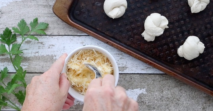 Parmesan Rhodes Rolls, a frozen dinner rolls recipe, showing frozen rolls on a baking sheet with a small white bowl of parmesan cheese being stirred.