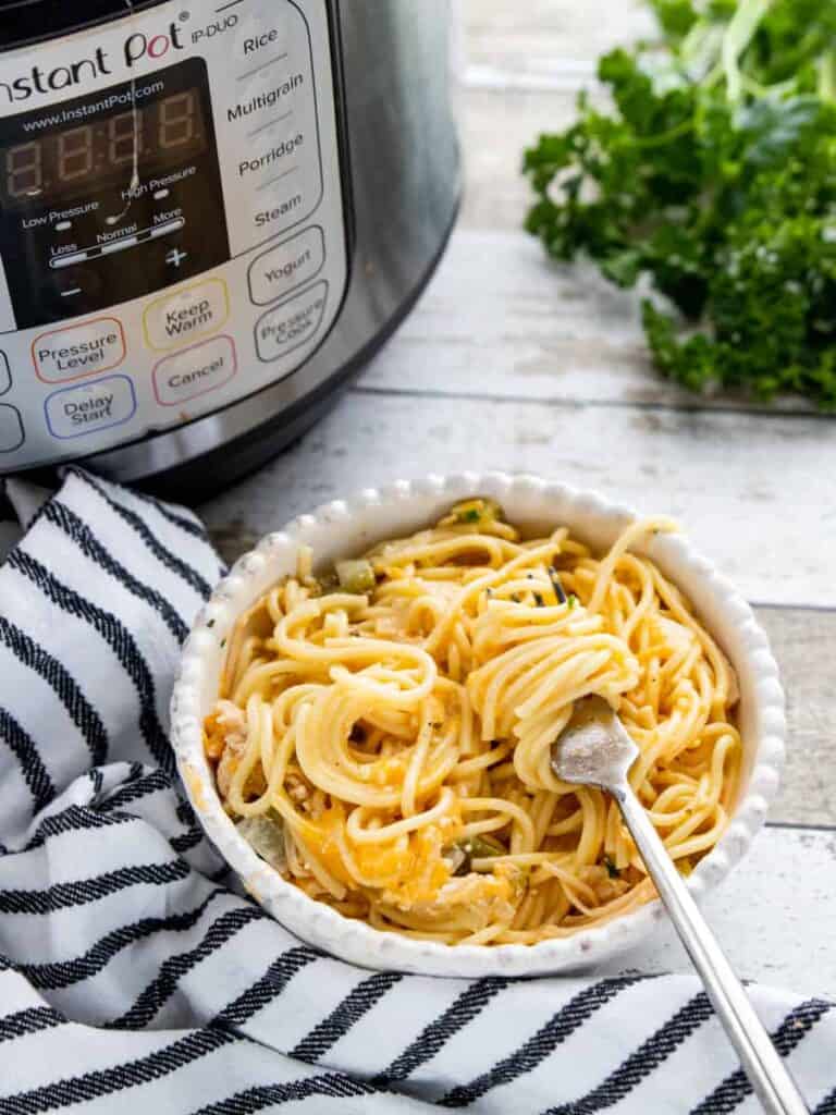 Instant Pot Chicken Spaghetti showing an instant pot, towel, parsley and a bowl of chicken spaghetti all on top of a wooden countertop.