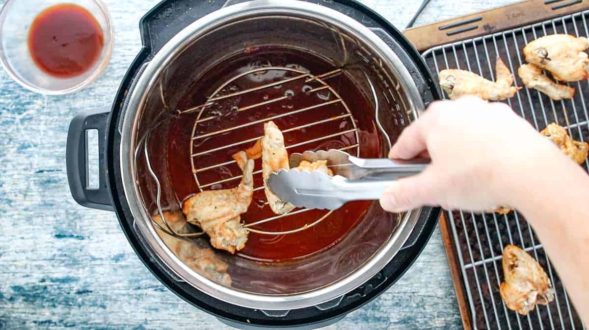 tongs scooping the cooked chicken wings from the instant pot and placing each wing on the wire rack that is on the baking sheet.