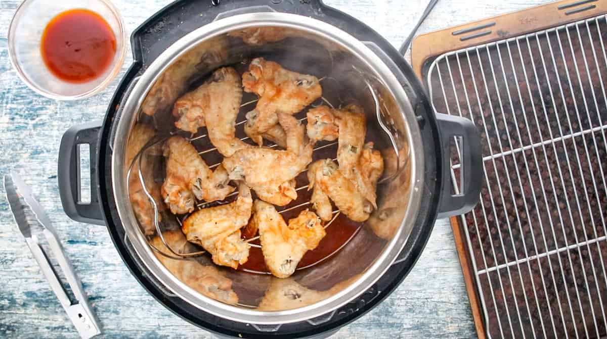 cooked chicken wings inside an instant pot with a baking sheet and wire rack by the side of the instant pot. 