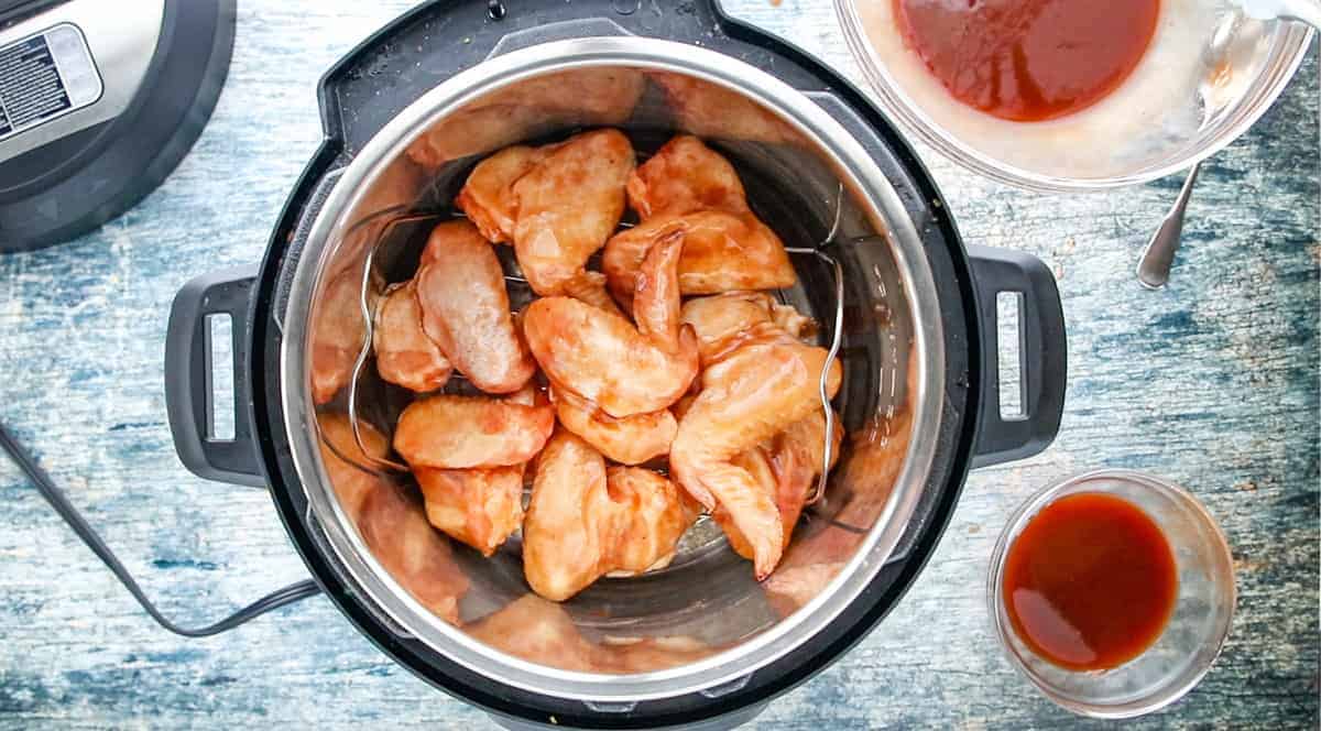 uncooked frozen chicken wings coated with bbq sauce on a wire rack inside an instant pot.