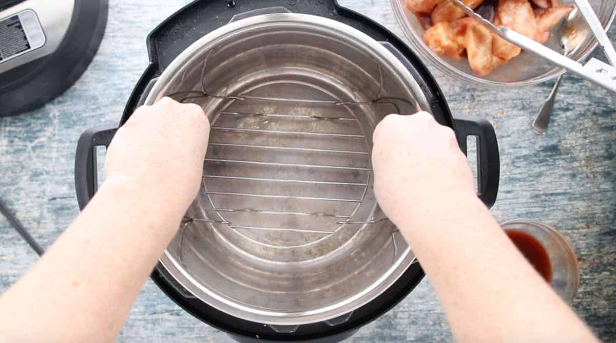 two hands placing a wire rack into an instant pot.