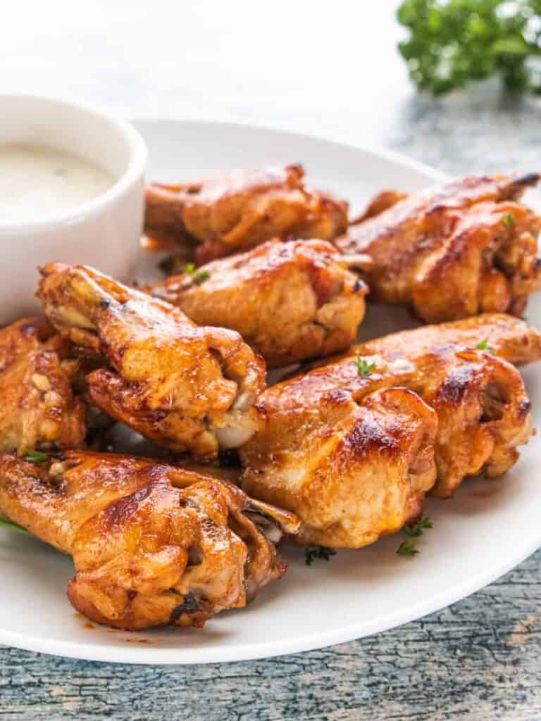 Chicken Wings being shown on a white plate with dipping sauce on the side.