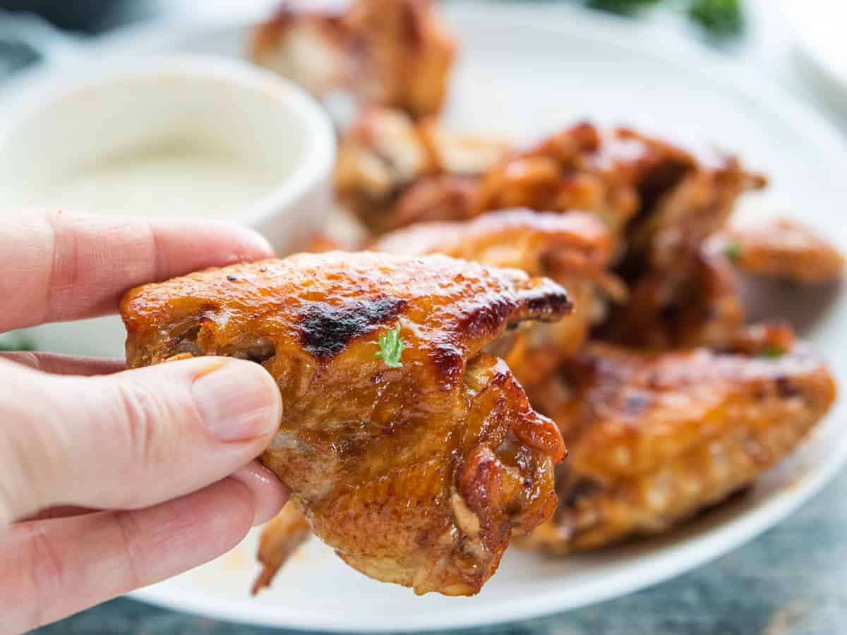  crispy wings on a plate with dipping sauce and a hand holding a chicken wing.