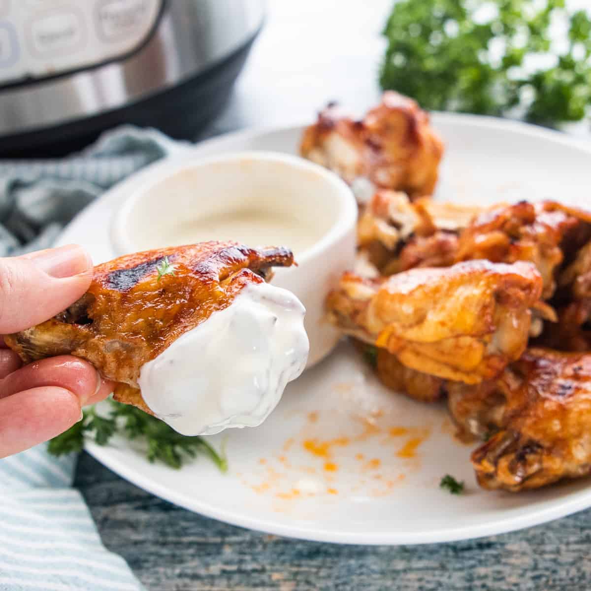 A crisp chicken wing dipped in blue cheese dressing shown up close with an instant pot in the background.