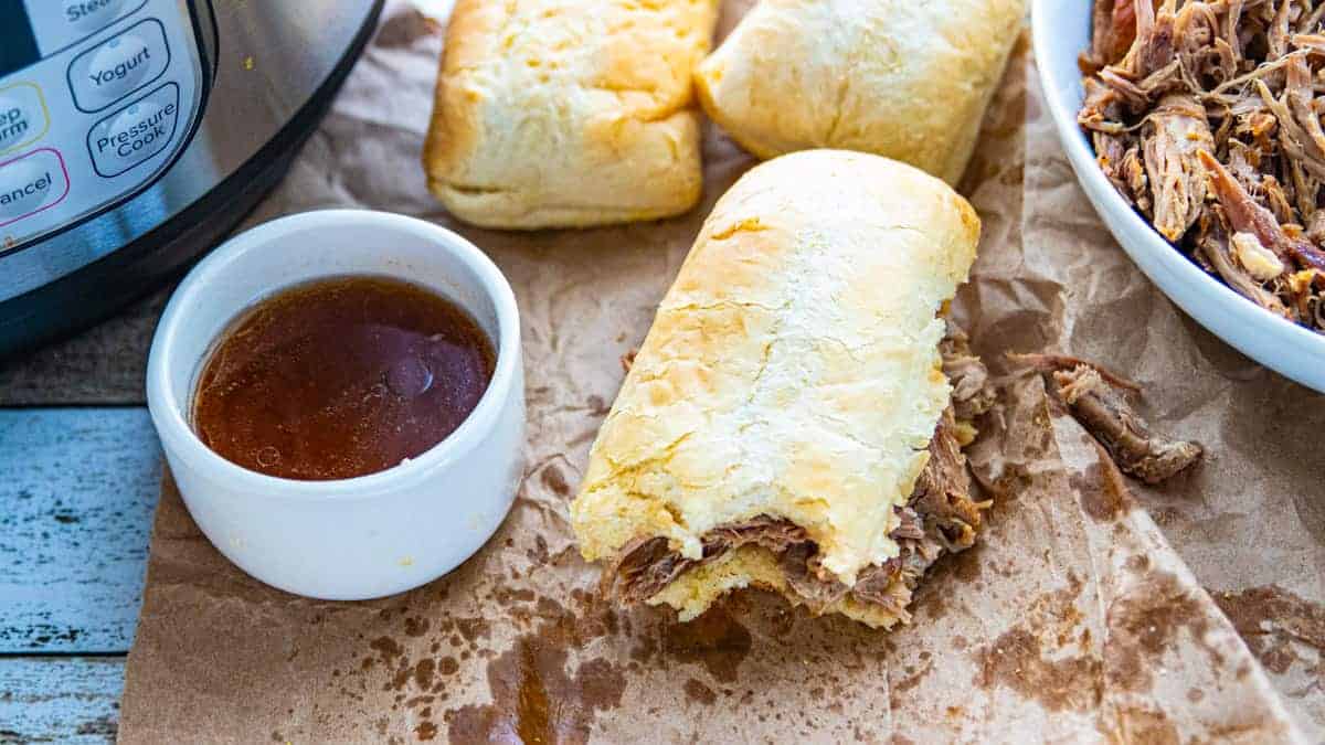 a French dip sandwich missing a bite with a side of au jus both on a countertop.