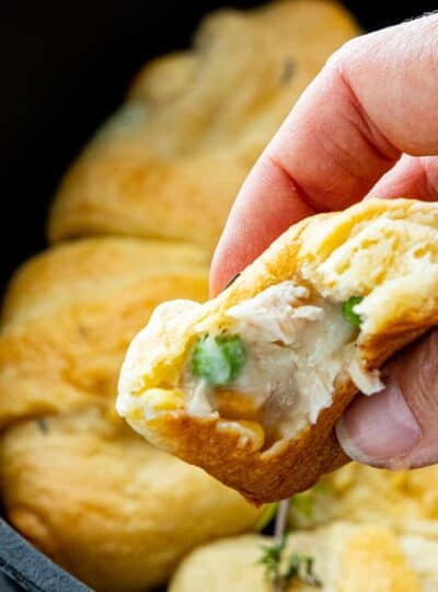 a hand is holding a pot pie stuffed crescent roll with more in the background.