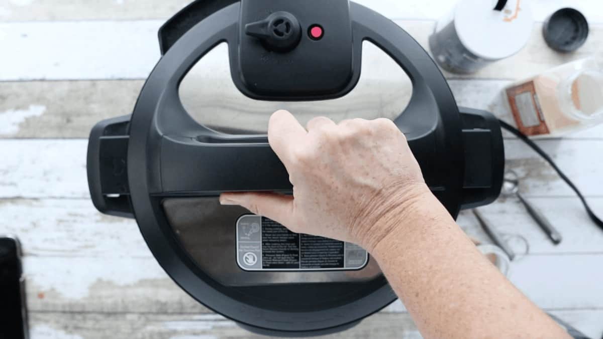 Instant pot cover shown with the float valve down and a hand ready to remove the lid.