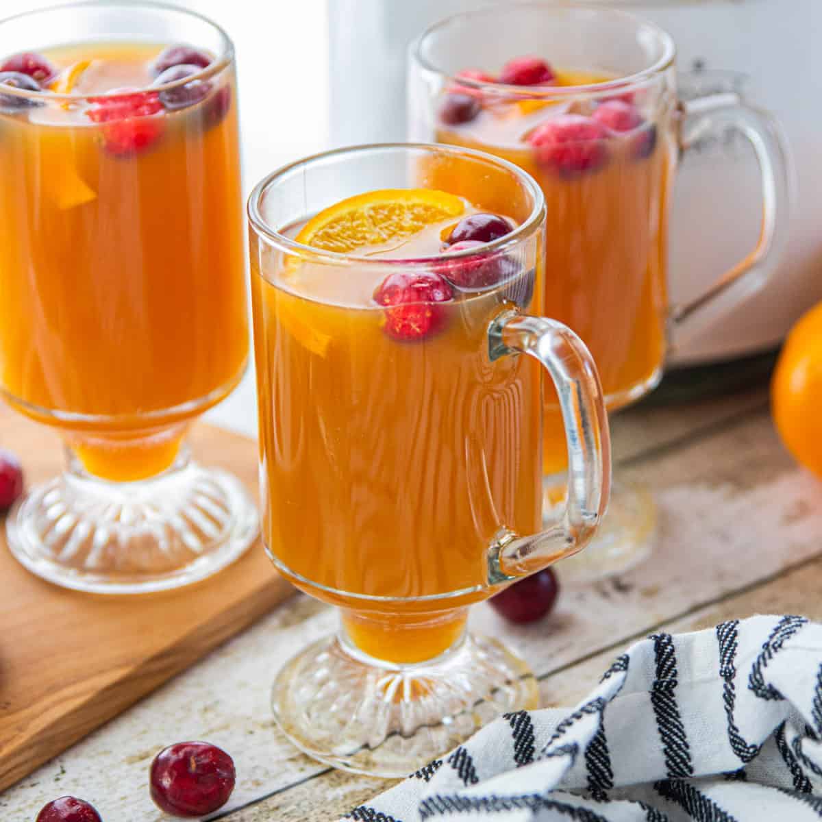 spiced apple cider in glass mugs with whole cranberries and orange slices.