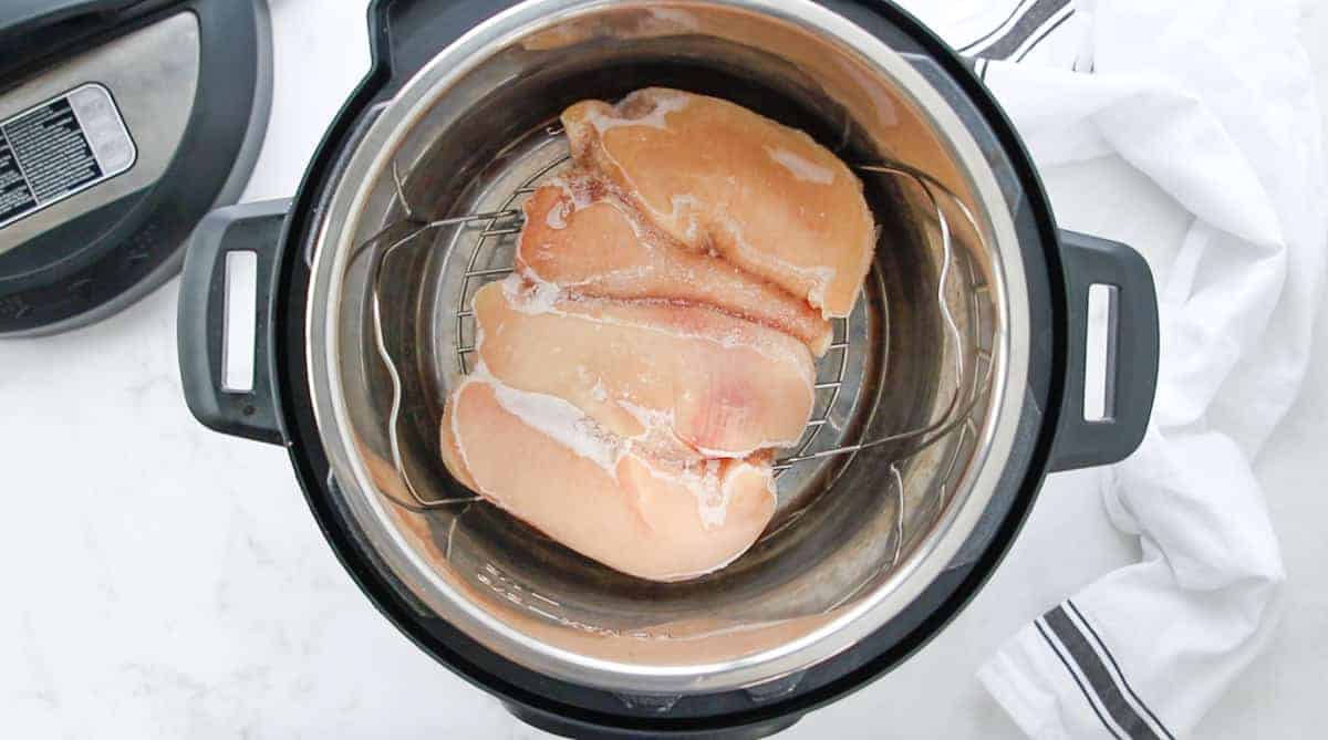 A top down view showing frozen chicken on a rack in an instant pot.