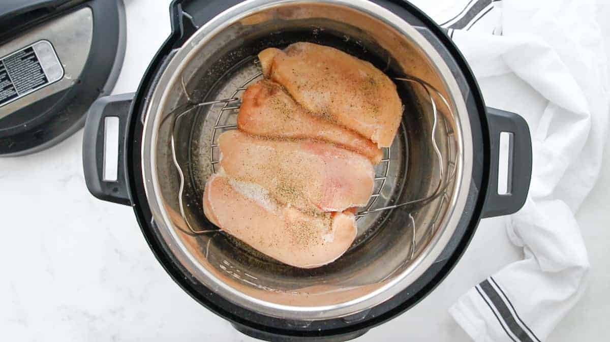 A top down view showing seasoned frozen chicken on a rack in an instant pot.