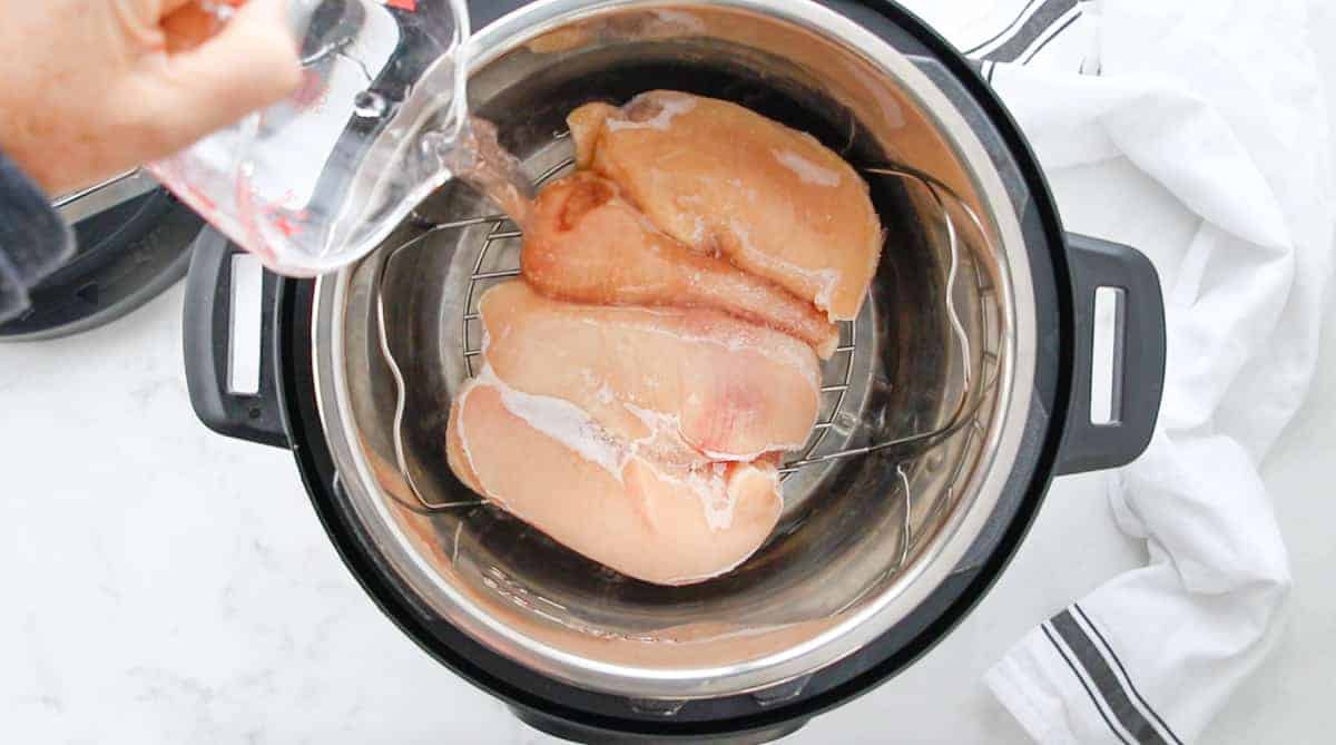 water being poured into the instant containing a wire rack and raw frozen chicken.
