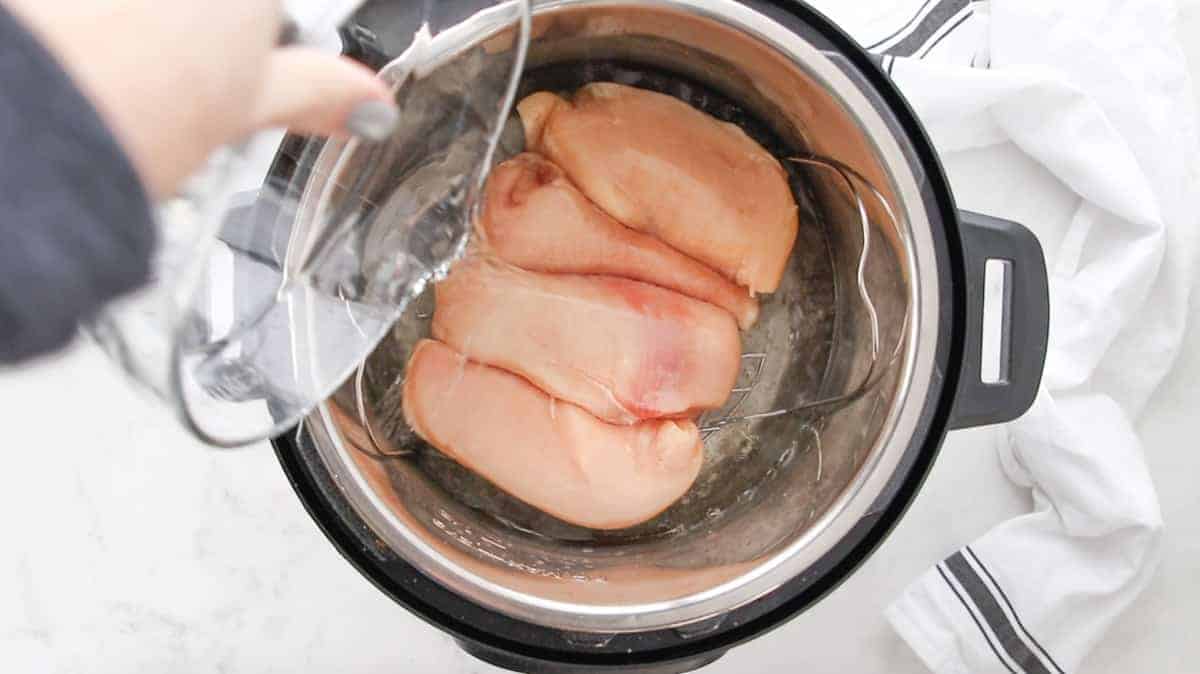 Top down view showing water being poured next to chicken on a rack in an instant pot.