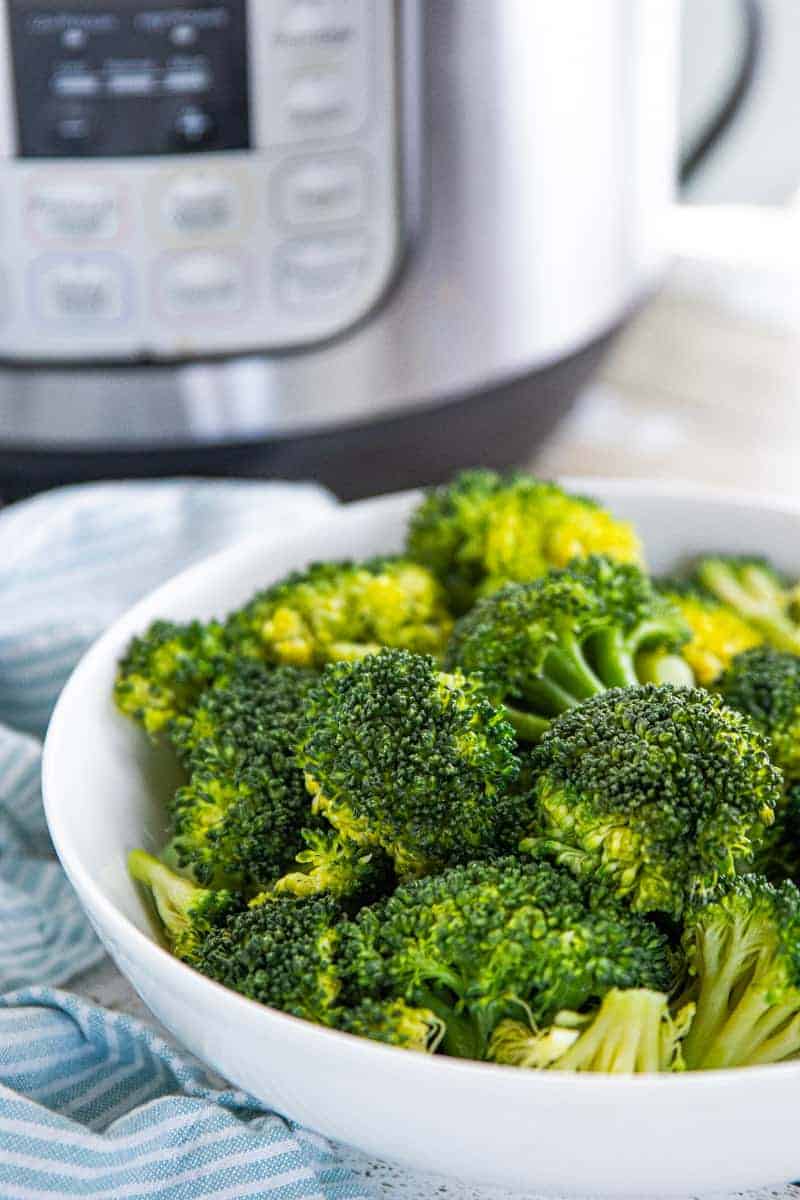 Steamed broccoli in a white serving bowl with an instant pot behind the bowl.