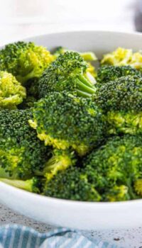 A white bowl filled with steamed broccoli on a white surface.