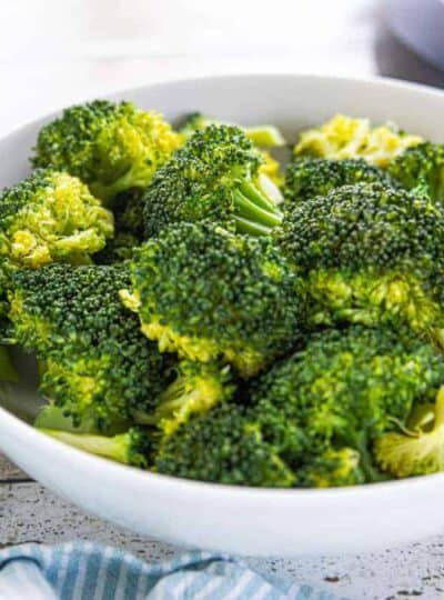 A white bowl filled with steamed broccoli on a white surface.