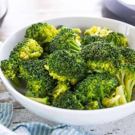 A white bowl filled with steamed broccoli on a white surface.