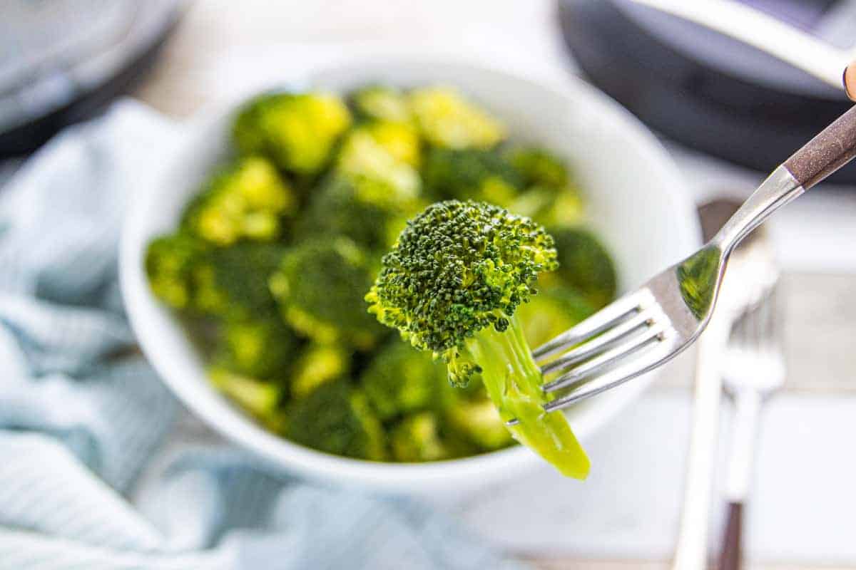 Instant Pot Broccoli showing steamed broccoli in a white bowl with a silver fork picking up one broccoli floret.