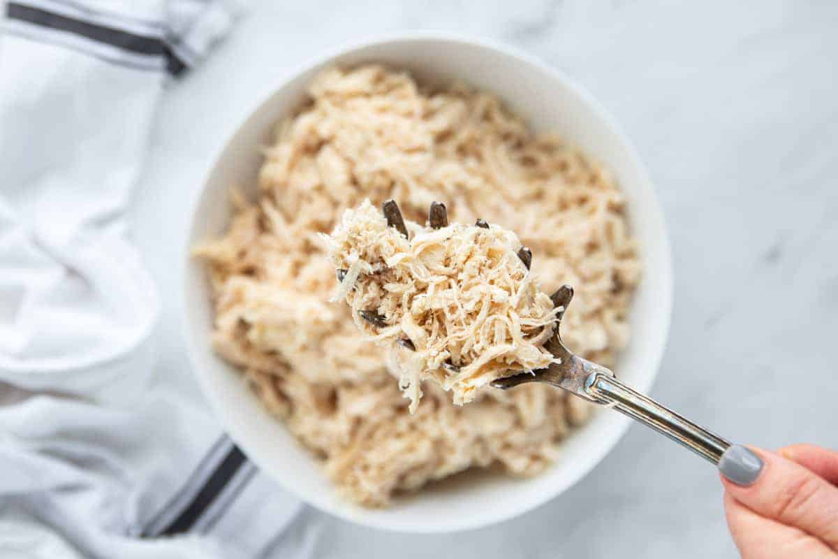 shredded chicken in a white bowl with a serving spoon scooping a serving of chicken.