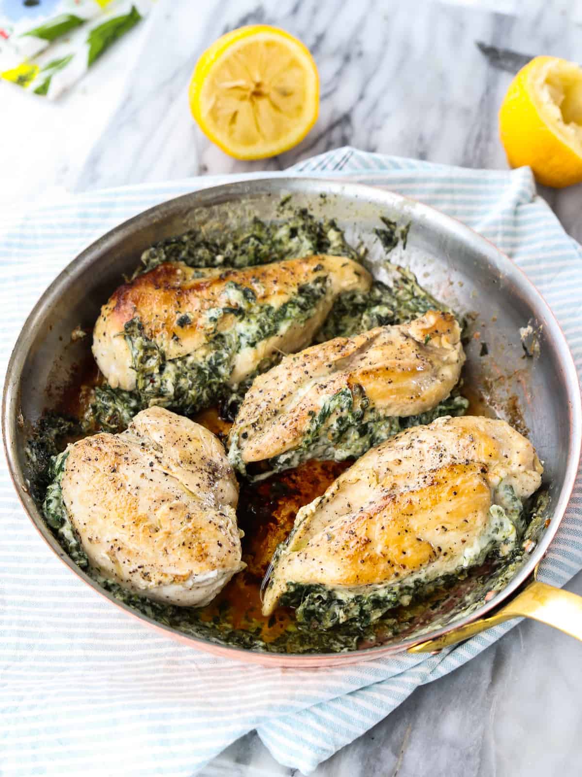Four cooked chicken breasts stuffed with a creamy spinach mixture in a skillet.