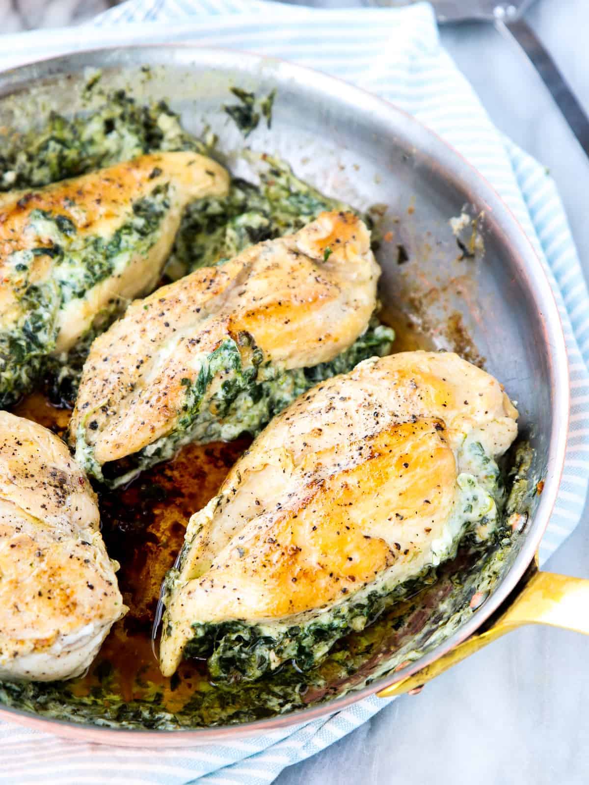 four cooked chicken breasts in a skillet stuffed with a spinach mixture and seasoned with pepper on top.