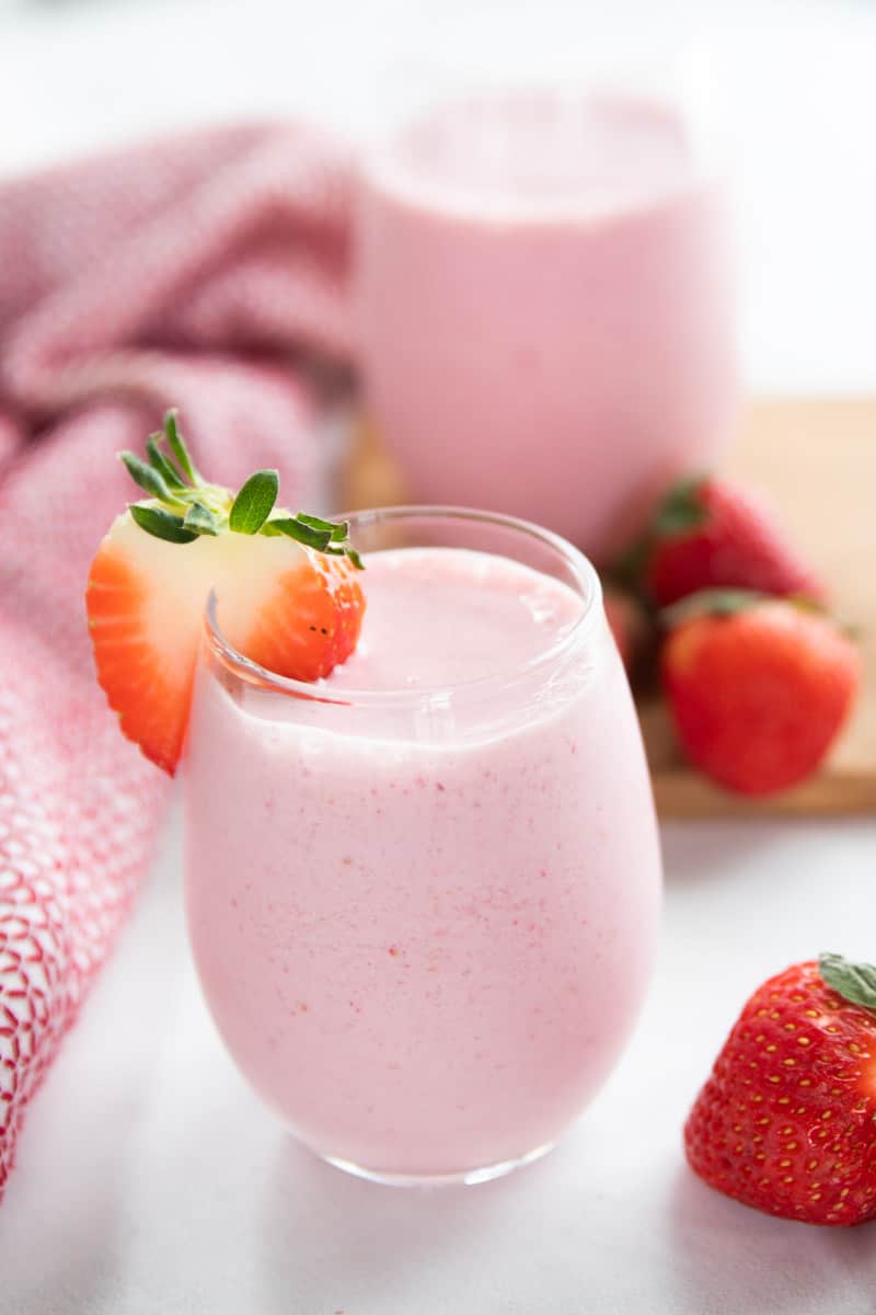 Strawberry Smoothie shown in a clear glass with a half a strawberry on the side of the glass.