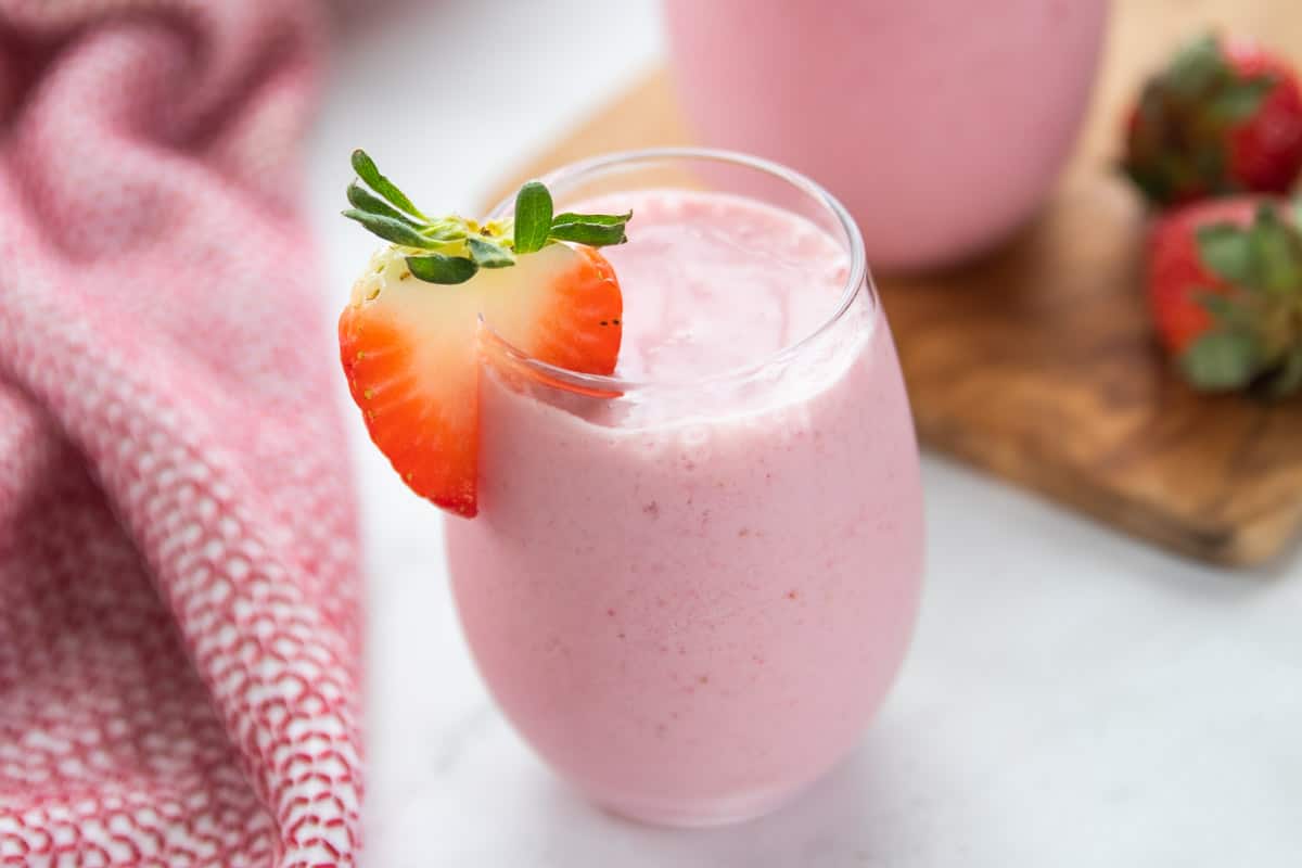Strawberry Smoothie Without Yogurt showing a smoothie in a glass with half a strawberry on the side of the glass.