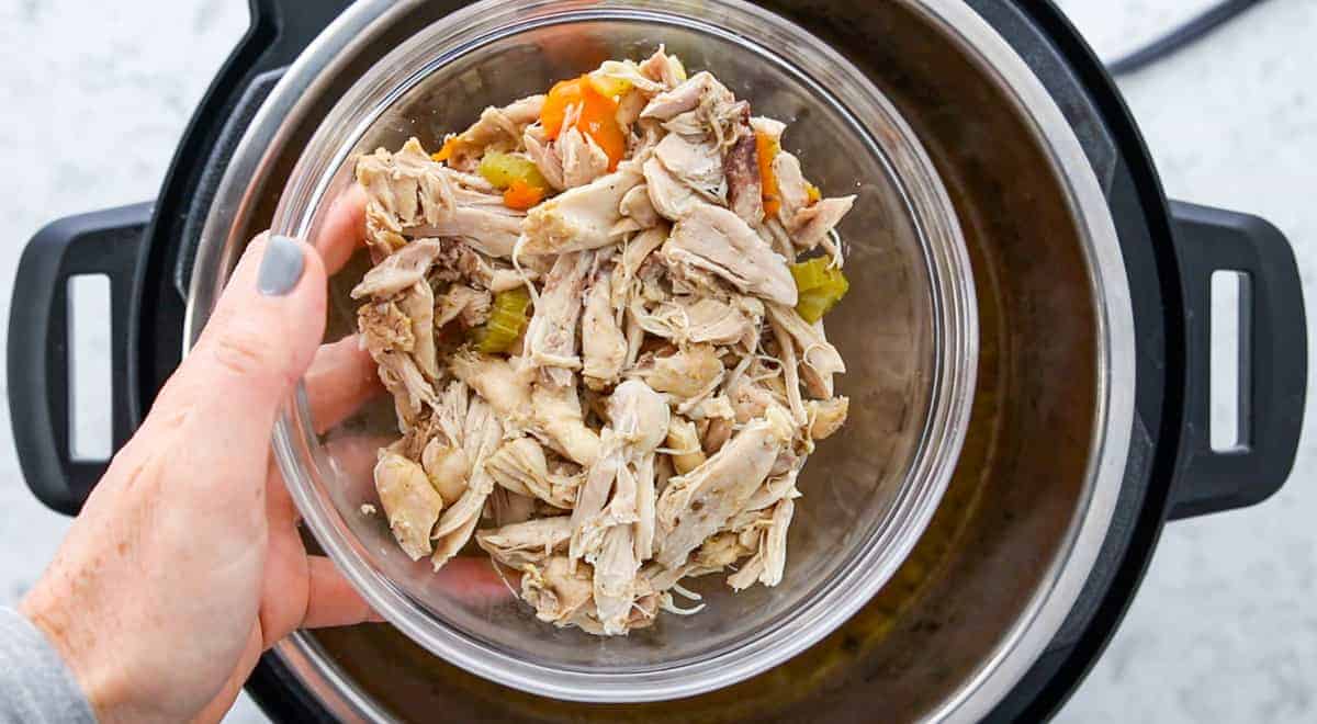 Instant Pot Chicken & Rice Soup showing shredded chicken being added to an instant pot.