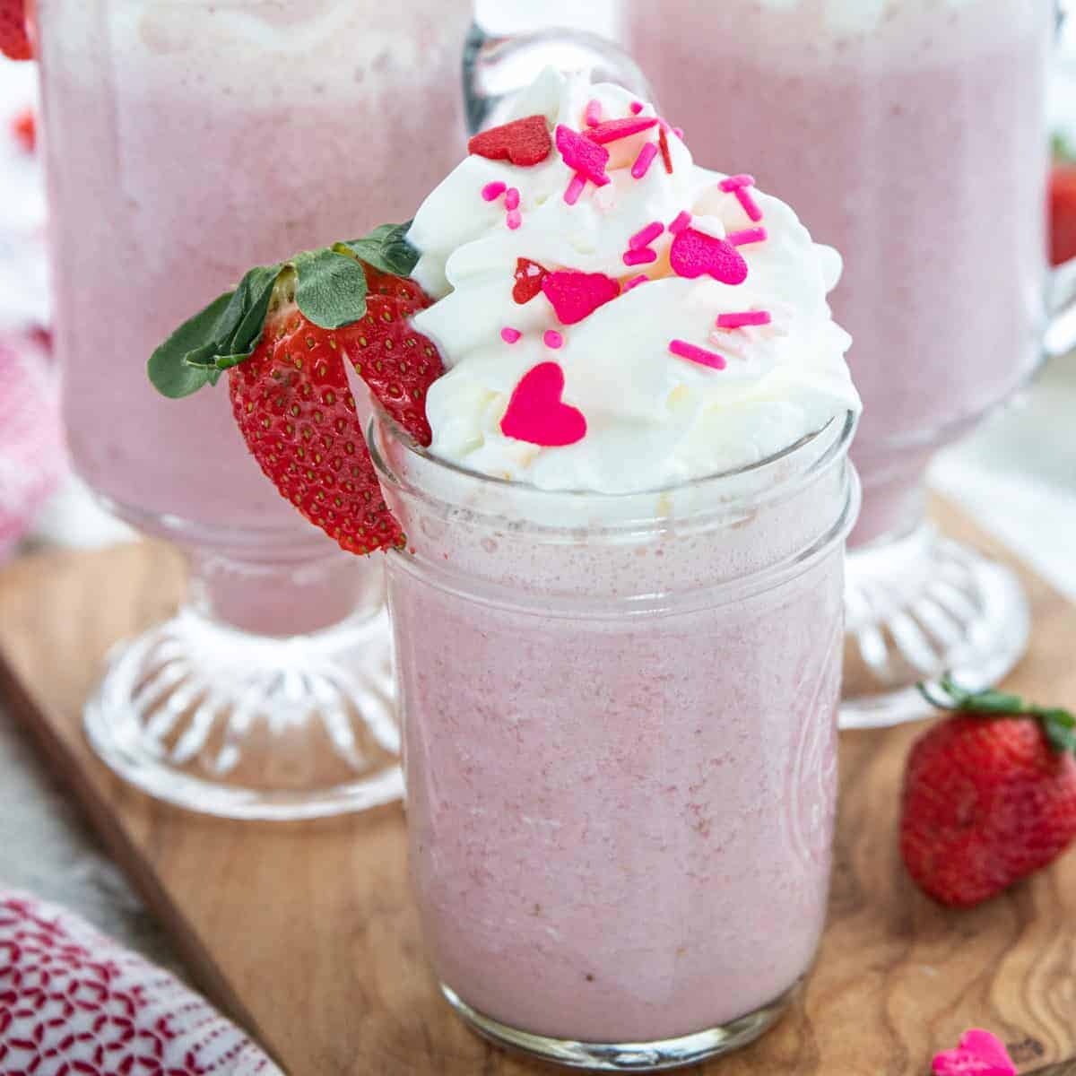 pink hot chocolate in a glass mug topped with whipped cream and a fresh strawberry.