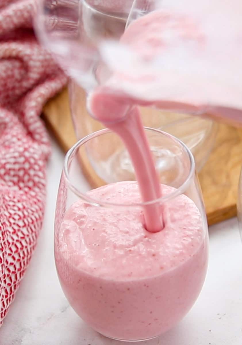 Strawberry smoothie being poured into a glass with a reusable straw.