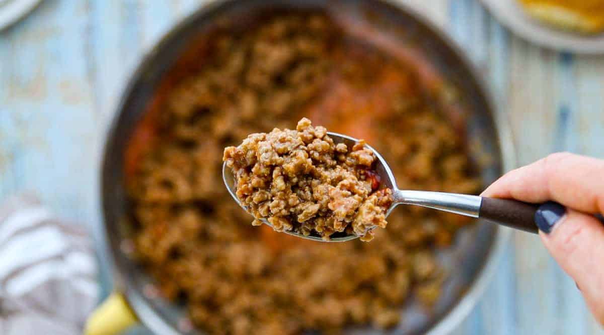 sloppy Joes in a skillet with a spoon showing a scoop of meat.