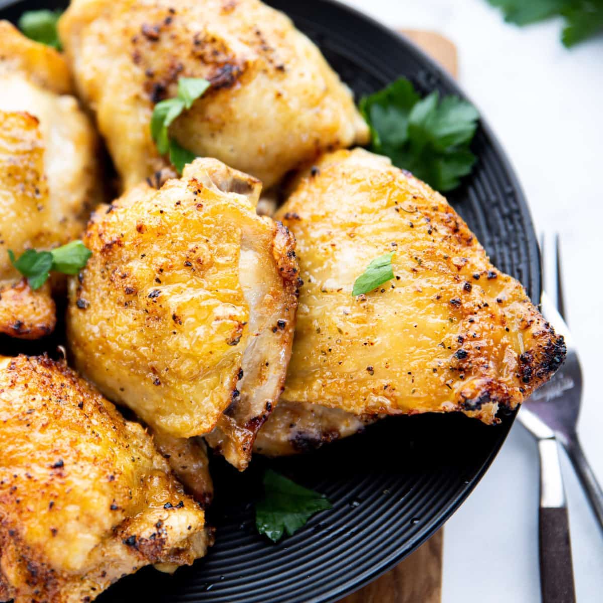 A close up shot of air fried chicken thighs on a black plate.